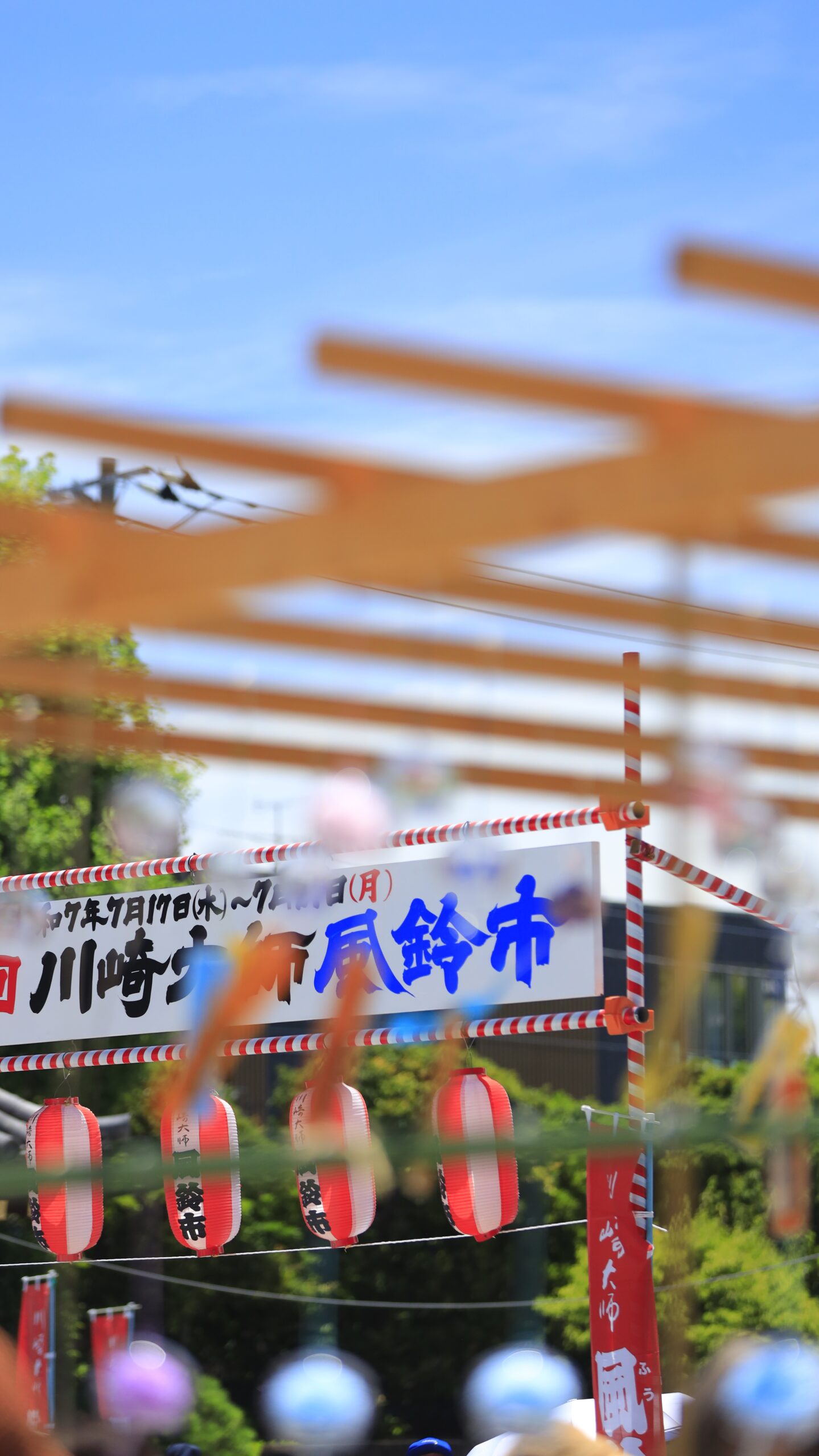 川崎大師の風鈴市で風鈴越しに設置された「風鈴位置」案内看板を撮影し、会場の雰囲気を伝える構図。