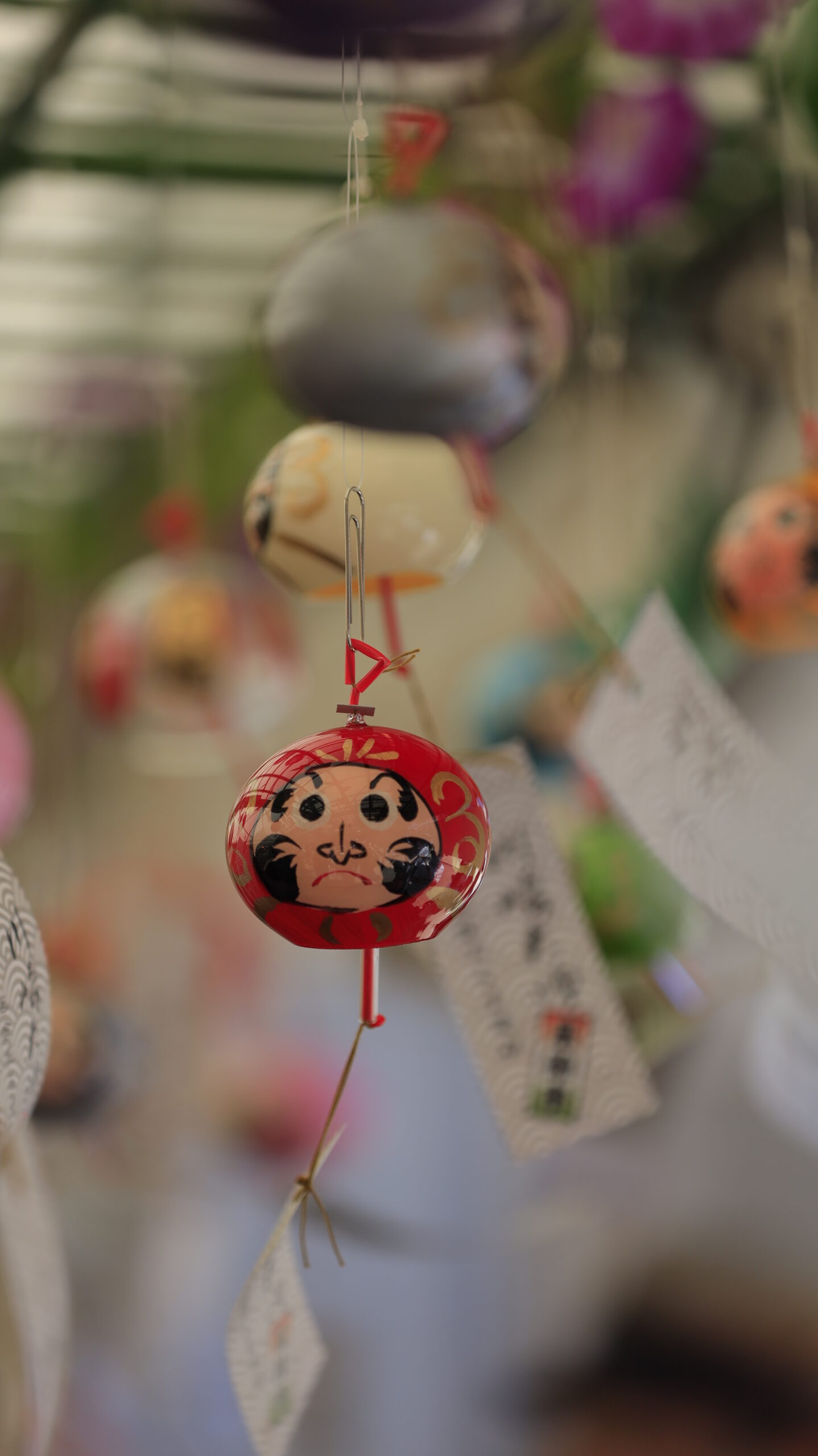 川崎大師の風鈴市で鮮やかな赤色の達磨風鈴が揺れる様子を中心にとらえ、存在感とかわいらしさを強調。