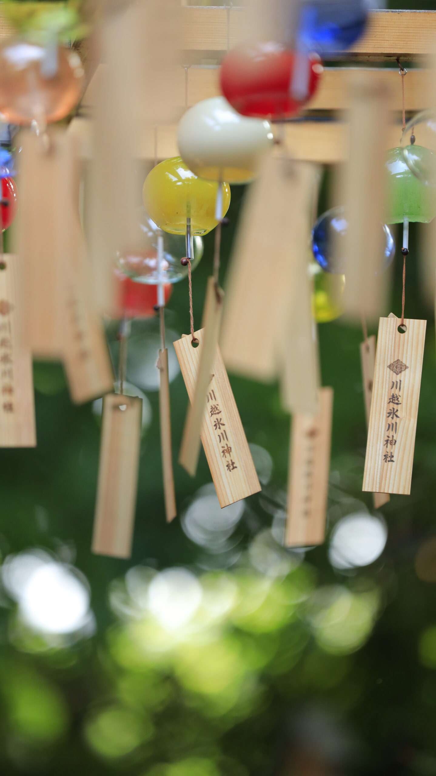 川越氷川神社で風にそよぐ風鈴のお札と玉ボケの緑を背景にした印象的な写真